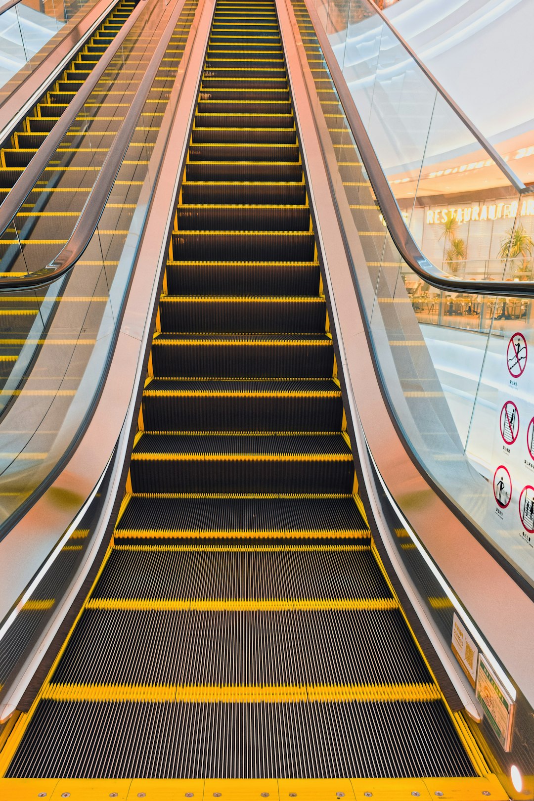 Escalator view in a modern shopping mall showing a unique perspective and lighting during daylight hours - A bright escalator leads upward in a contemporary shopping mall. The light reflects on the escalator, creating an inviting atmosphere for shoppers.