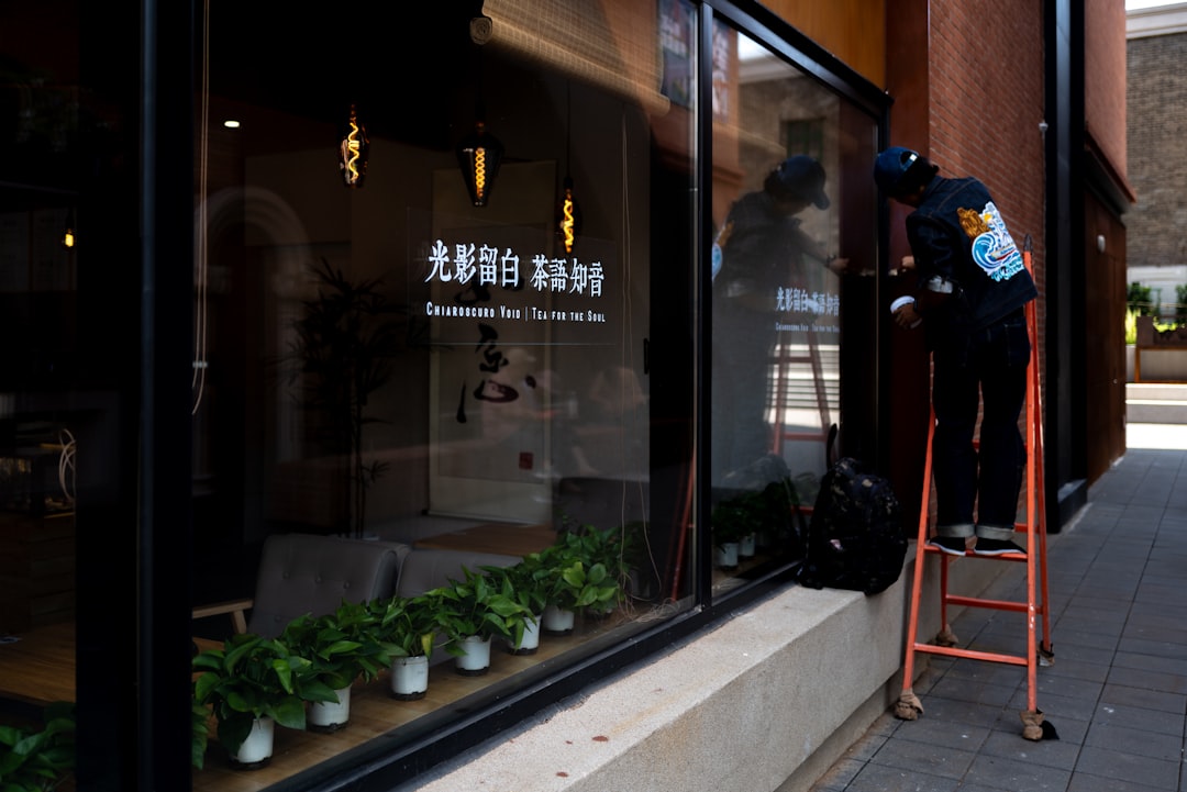 Person cleaning window on a ladder outside building exterior